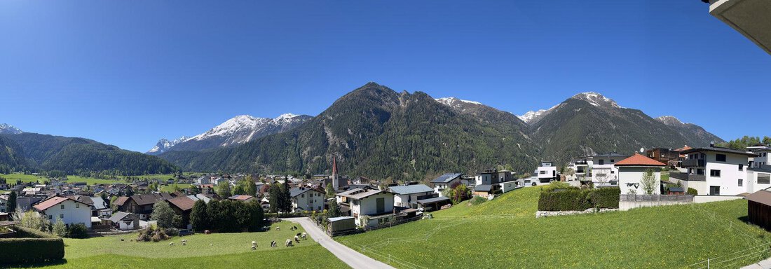 Eine malerische Landschaft mit Bergen im Hintergrund und einem klaren blauen Himmel. Im Vordergrund sind grüne Wiesen und einige Wohnhäuser zu sehen. - BLANKA'S Apart Auszeit - Umhausen