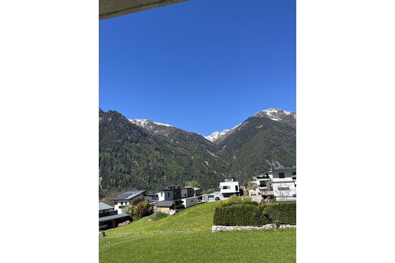 Eine beeindruckende Berglandschaft mit schneebedeckten Gipfeln und einem klaren blauen Himmel. Im Vordergrund sind moderne Häuser und grüne Wiesen zu sehen. - BLANKA'S Apart Auszeit - Umhausen