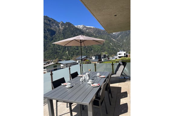 Ein schöner Balkon mit einem modernen Tisch und Stühlen. Im Hintergrund sind grüne Berge und eine klare Himmel zu sehen. - BLANKA'S Apart Auszeit - Umhausen