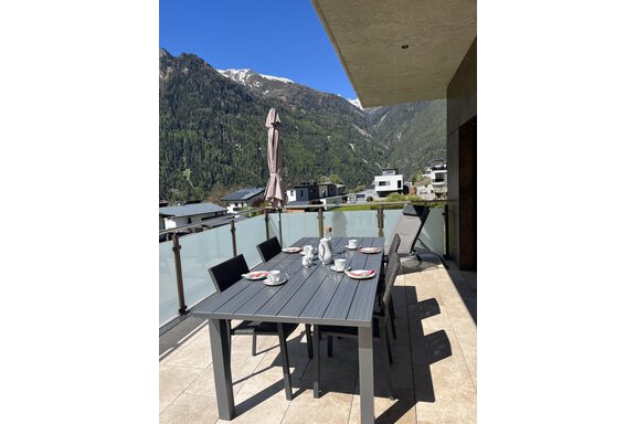Ein schöner Balkon mit einem Esstisch und Stühlen. Im Hintergrund sind grüne Berge und ein klarer blauer Himmel zu sehen. - BLANKA'S Apart Auszeit - Umhausen