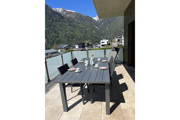 Ein eleganter Esstisch auf einer Terrasse mit Blick auf die Berge. Der Tisch ist festlich gedeckt mit Geschirr und Besteck. - BLANKA'S Apart Auszeit - Umhausen