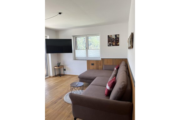 Ein modernes Wohnzimmer mit einem bequemen Sofa und einem Fernseher an der Wand. Helle Fenster lassen viel Licht herein und es gibt dekorative Elemente an den Wänden. - BLANKA'S Apart Auszeit - Umhausen