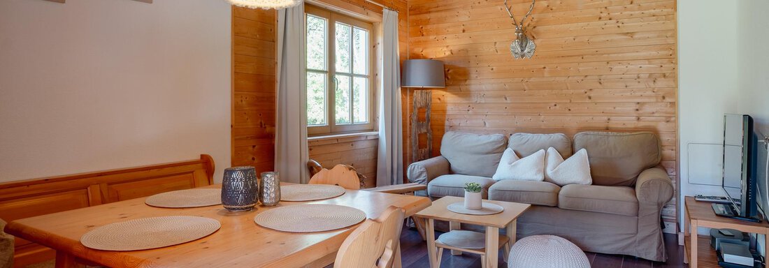 A cozy living room with wooden walls and a large sofa.  
The table is set and windows let in a lot of light. - Chalet Carla - Umhausen