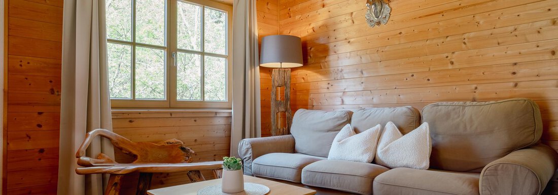 A cozy living room with wood paneling. There is a comfortable sofa, a table, and large windows that let in plenty of light. - Chalet Carla - Umhausen