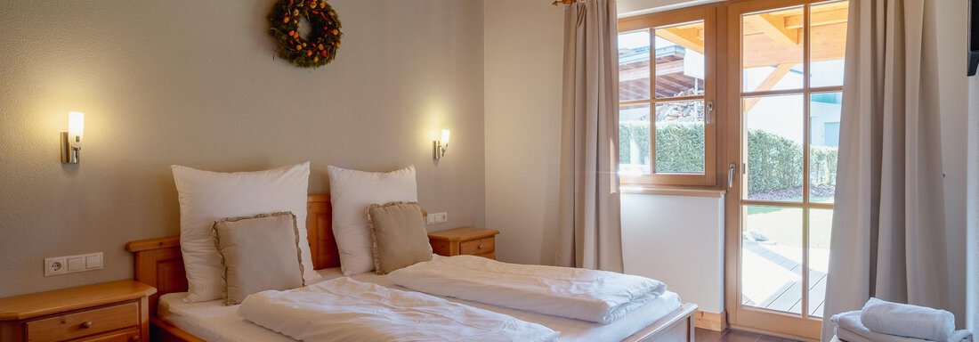 A cozy bedroom with a double bed and wooden décor. Large windows let in plenty of daylight and provide a view of the outdoors. - Chalet Carla - Umhausen