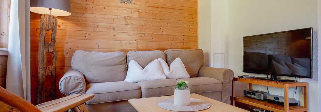 A cozy living room with a beige sofa, a wooden table, and a television. The walls are covered with wood, creating a warm atmosphere. - Chalet Carla - Umhausen