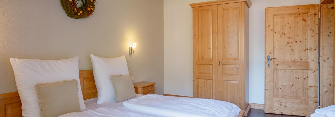 A cozy bedroom with two beds and wood-paneled walls. The room has a warm atmosphere and a rustic wardrobe. - Chalet Carla - Umhausen