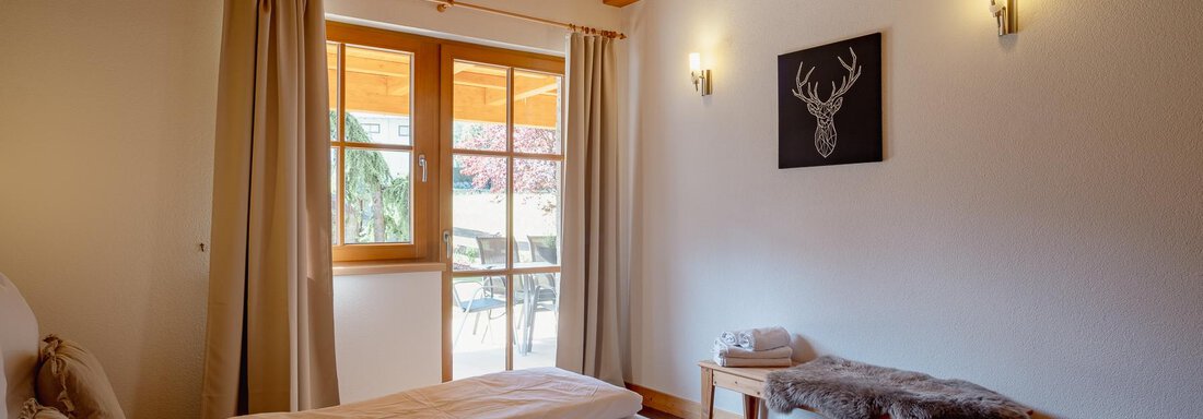 A cozy bedroom with wooden ceilings and a large window. The room has two separate beds and a rustic decoration. - Chalet Carla - Umhausen