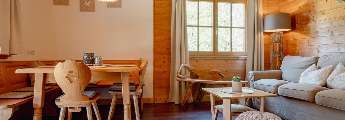 Chalet Carla - gemütliches Wohnzimmer | © Chalet Carla (CC C) A cozy living area with wood paneling and a large window. There is a dining room with a table and chairs, as well as a comfortable sofa. - Chalet Carla - Umhausen