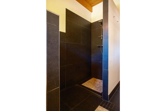 A modern shower cabin with dark tiles and a minimalist design. The shower has a clean, elegant look and plenty of space. - Chalet Carla - Umhausen