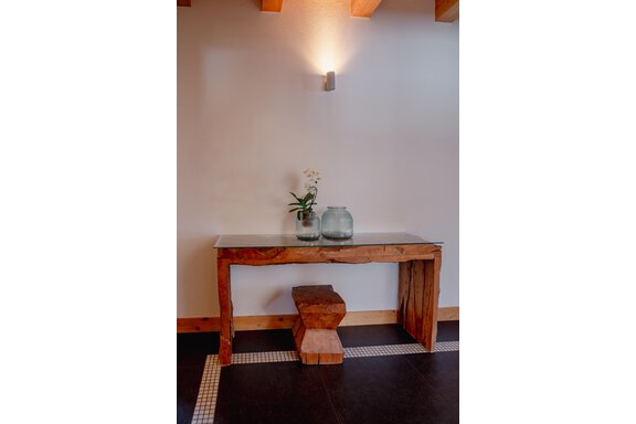 An elegant wooden table with a glass top and a wooden bench next to it. On the table sits a vase with a plant and two glasses. - Chalet Carla - Umhausen