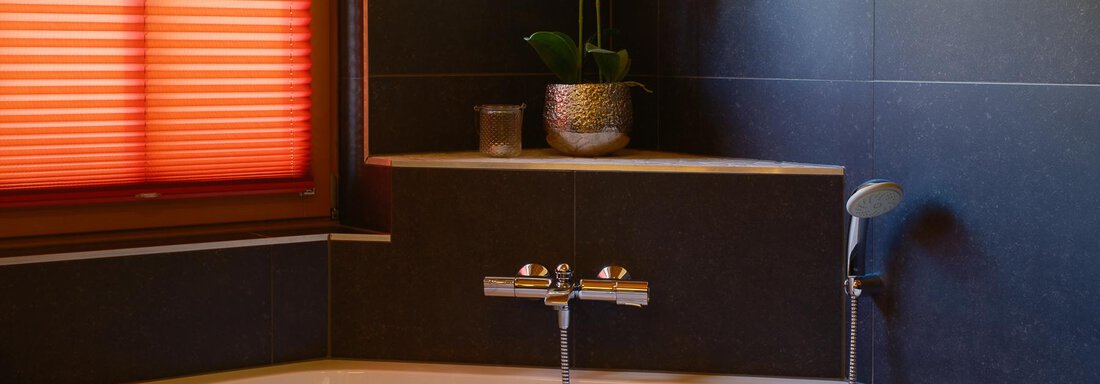A modern bathroom with an elegant bathtub. The red-orange pleated curtains and an orchid plant give the room a cozy atmosphere. - Chalet Carla - Umhausen