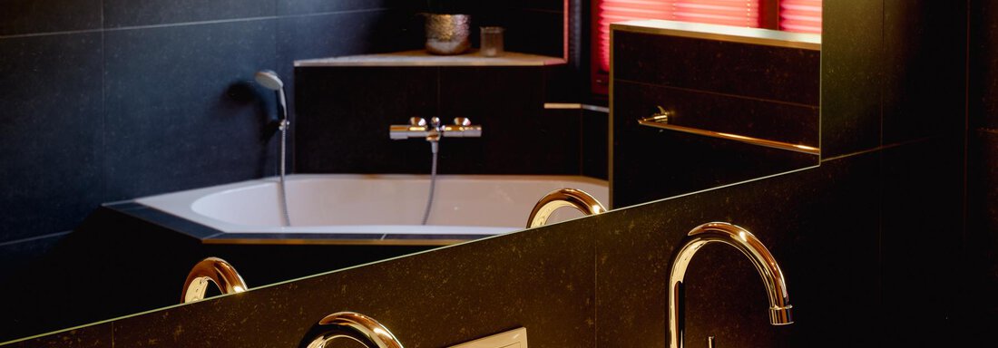 A modern bathroom with a black tiled wall and a bathtub. In the foreground, elegant faucets and decorative elements are visible. - Chalet Carla - Umhausen