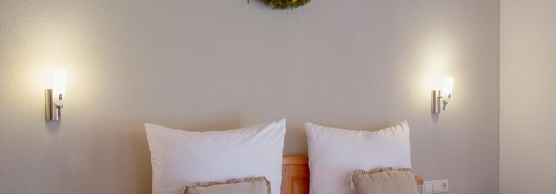 A cozy bedroom with two beds and light-colored pillows. A decorative wreath hangs on the wall. - Chalet Carla - Umhausen