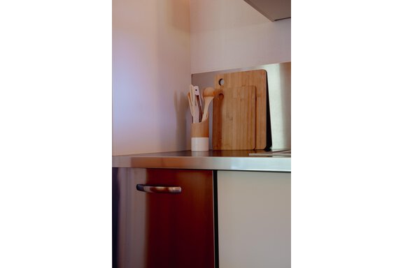 A modern kitchen with wooden utensils. On the countertop, there is a cutting board and a container for cooking spoons. - Chalet Carla - Umhausen