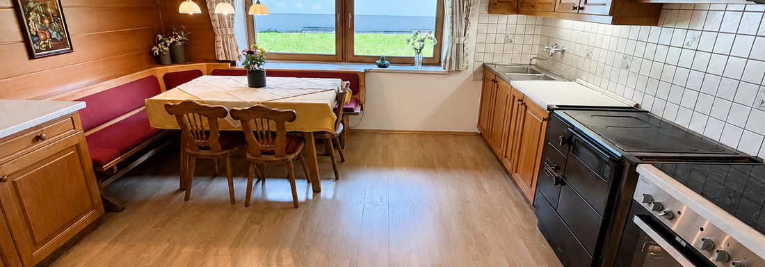 A cozy kitchen with wooden cabinets and a dining table. The window offers a view of the greenery. - Ferienhaus am Spielroan - Umhausen