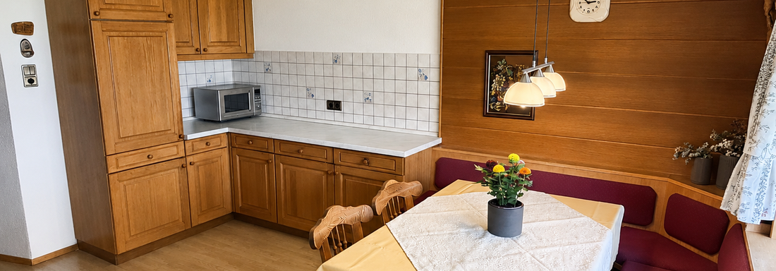 A cozy kitchen with wooden cabinets and a dining table. In the corner, there is a bench with colorful cushions. - Ferienhaus am Spielroan - Umhausen
