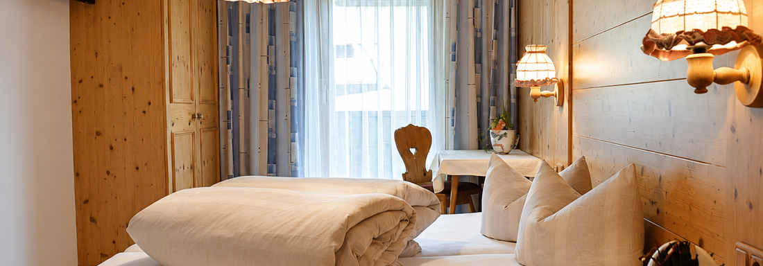 A cozy bedroom with wooden walls and warm colors. There are two beds, beautiful lamps, and a table with a chair. - Ferienhaus am Spielroan - Umhausen
