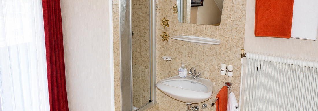 A modern bathroom with a shower, a sink, and a large mirror. The walls are bright and designed with decorative wallpaper, complemented by eye-catching towels. - Ferienhaus am Spielroan - Umhausen