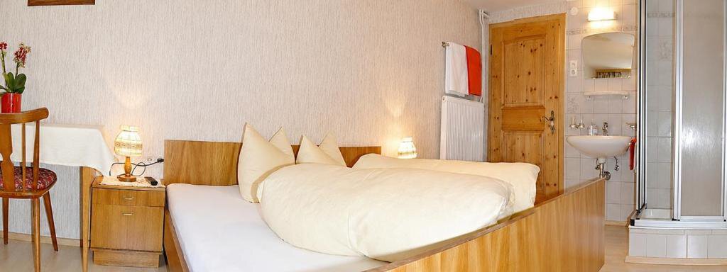 A cozy bedroom with a double bed and wooden details. In the background, there is a bathroom and a small seating area. - Ferienhaus am Spielroan - Umhausen