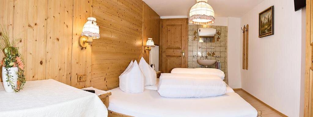 A cozy room with wooden paneling and a large bed. There is a tablecloth and humorous lamps for a warm atmosphere. - Ferienhaus am Spielroan - Umhausen