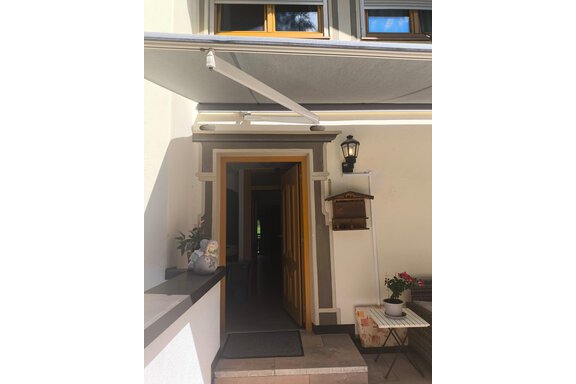An inviting entrance area with an open door and bright light. On the left, a small plant is on a table. - Ferienwohnung Martha - Umhausen