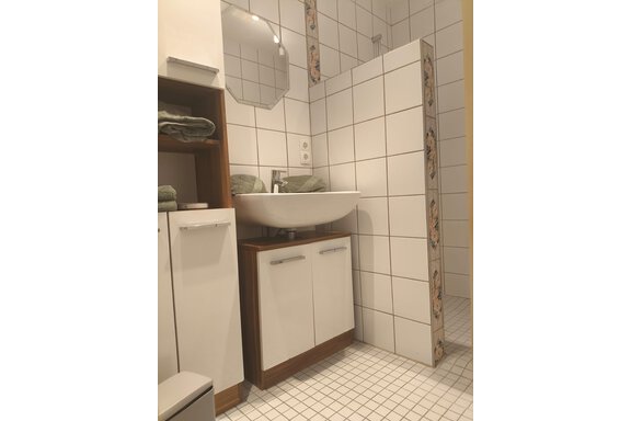 A modern bathroom with bright tiles and a shower. There is a sink with a cabinet and towels in soft colors. - Ferienwohnung Martha - Umhausen