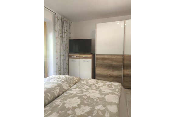A cozy bedroom with a double bed and bright bedding. In the background, there is a television next to a modern wardrobe. - Ferienwohnung Martha - Umhausen