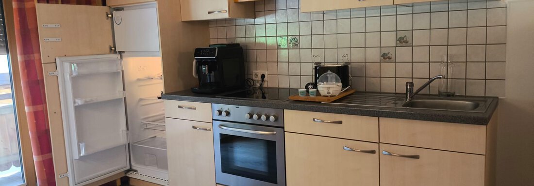 A modern kitchen with wooden cabinets and bright tiles. The room is well lit and features appliances such as a refrigerator and an oven. - Ferienwohnung Martha - Umhausen