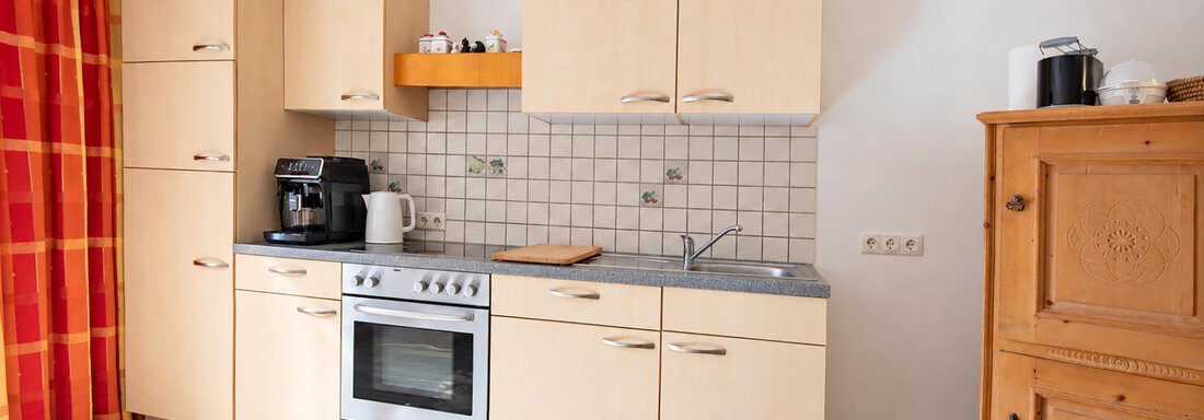 A modern kitchen with bright wooden cabinets and an oven. There is a cozy atmosphere with natural light and a window. - Ferienwohnung Martha - Umhausen