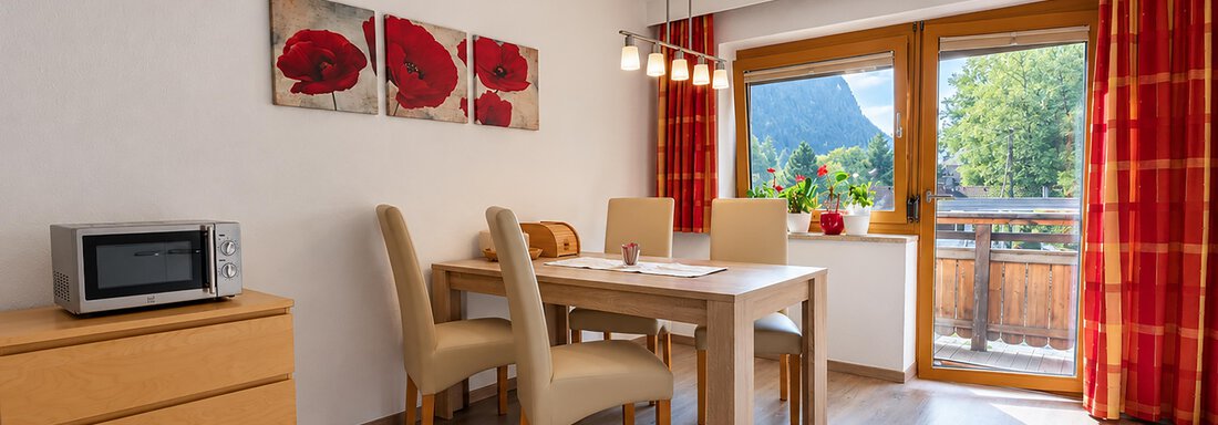 A bright dining room with a table and four chairs. Large windows provide a view of nature and let in plenty of light. - Ferienwohnung Martha - Umhausen