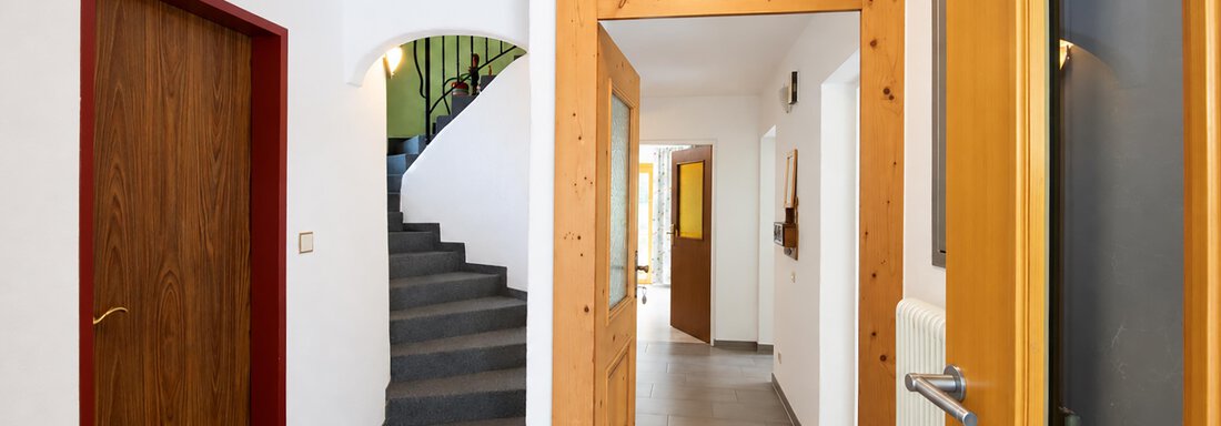 A bright corridor with wooden and glass doors. In the background, a staircase and additional doors can be seen. - Ferienwohnung Martha - Umhausen