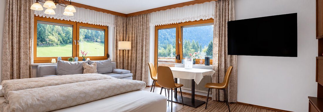 A cozy bedroom with a large bed and a beautiful view of the mountains. The room is bright and modernly furnished with a dining area and a television. - Ferienwohnung Martha - Umhausen