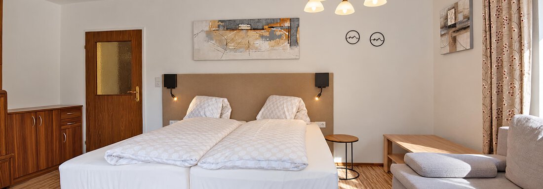 A cozy hotel room with two single beds and a modern sofa. The room is bright and cheerful, with a beautiful pendant light and decorations on the walls. - Ferienwohnung Martha - Umhausen