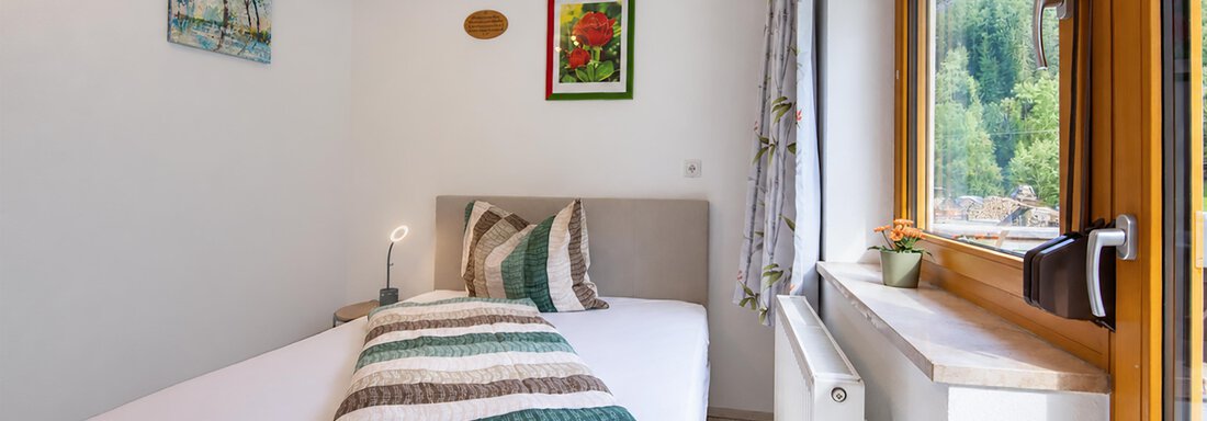 A simple bedroom with a single bed and colorful wall murals. A window lets in plenty of daylight and offers a view outside. - Ferienwohnung Martha - Umhausen