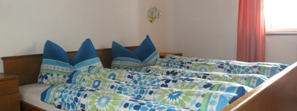 A cozy bedroom with a large double bed and colorful blankets. The windows are decorated with red curtains and let in a lot of light. - Appt. Garni Anny - Vent