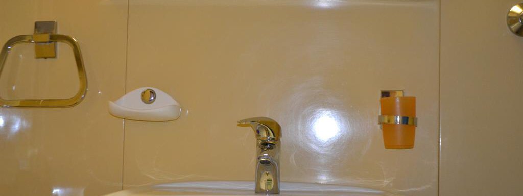 A modern bathroom with a sink and a small shelf. On the shelf, there is an orange lamp and two handy containers placed. - Appt. Garni Anny - Vent