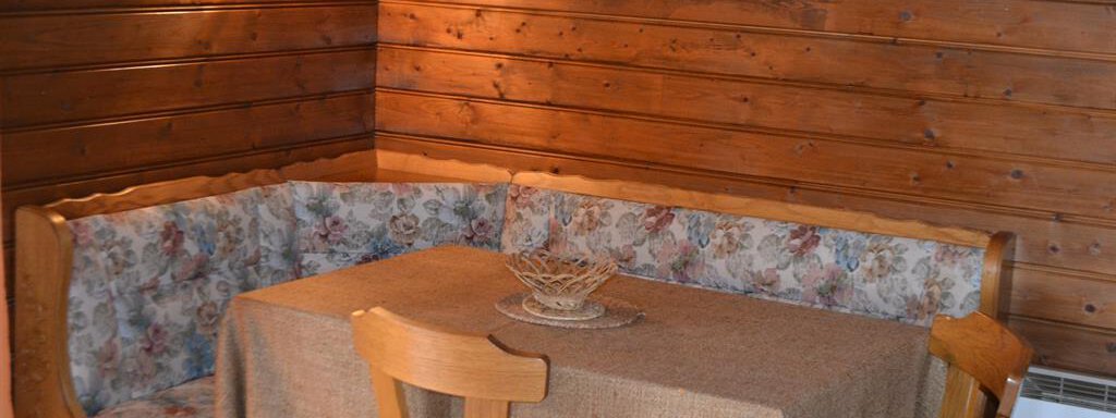 A cozy dining area with wood paneling and a bench. The table is set with a natural cloth and a decorative bowl. - Appt. Garni Anny - Vent