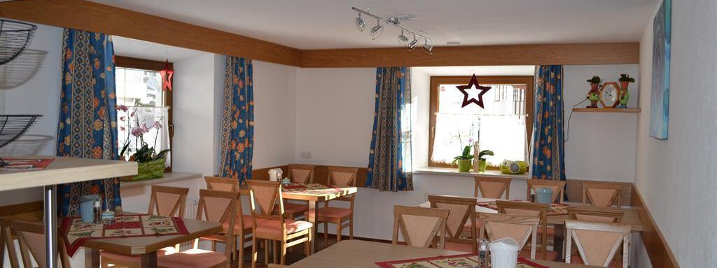 A cozy dining area with wooden chairs and tables. The walls are painted light, and colorful curtains create an inviting atmosphere. - Appt. Garni Anny - Vent