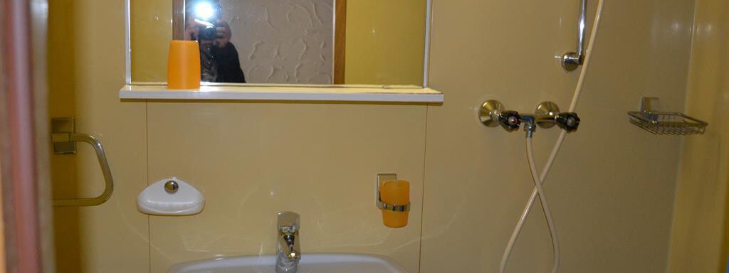 A small bathroom with a sink and a mirror. The walls are painted in a light shade of yellow. - Appt. Garni Anny - Vent