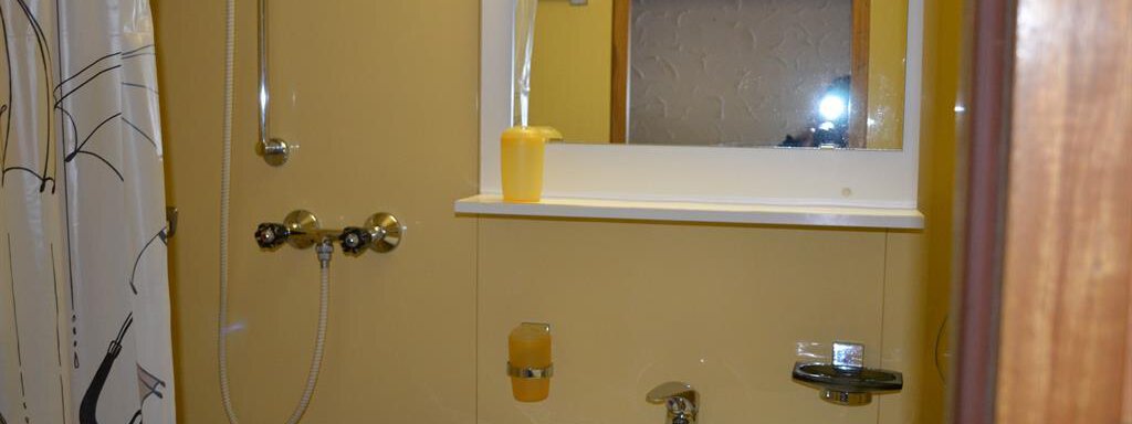 A bathroom with yellow walls and a sink. The shower has a shower curtain and there is a mirror above the sink. - Appt. Garni Anny - Vent