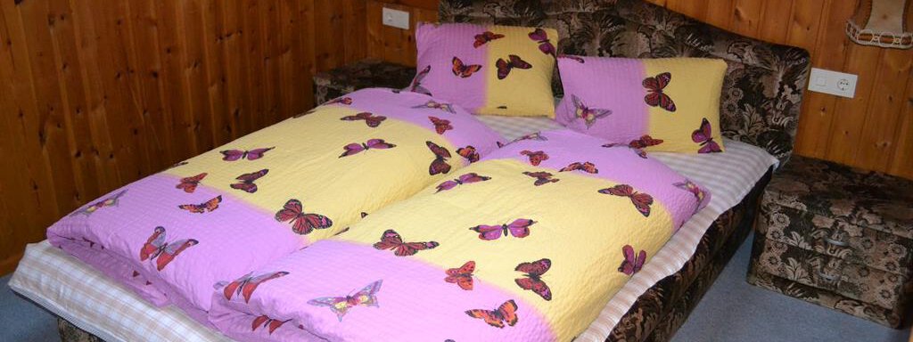 A cozy bedroom with a double bed. The bedding is colorful with butterflies, and the walls are made of wood. - Appt. Garni Anny - Vent