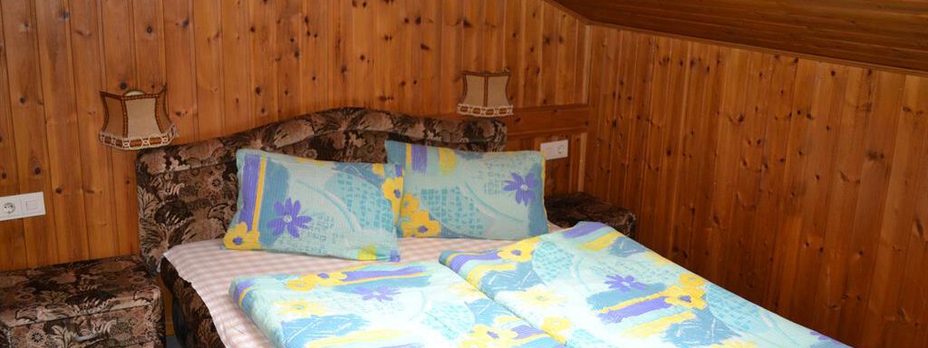 A cozy bedroom with wooden walls and a double bed. The bedding is colorful and the atmosphere is warm and inviting. - Appt. Garni Anny - Vent