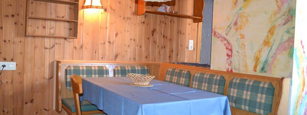 A cozy dining area in a wooden room with a blue tablecloth. The walls are clad in wood and there is a ceiling lamp. - Appt. Garni Anny - Vent
