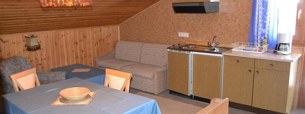 A cozy holiday apartment with wooden walls and a large window. The room features a dining area, a couch, and a small kitchenette. - Appt. Garni Anny - Vent