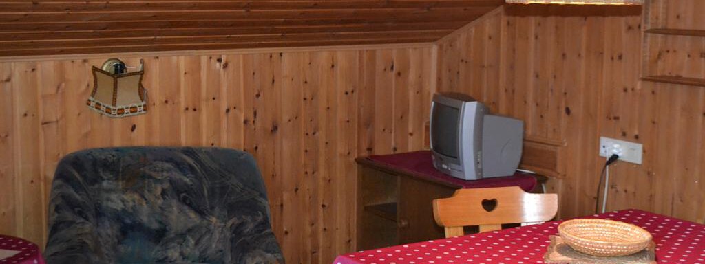 A cozy room with wooden paneling and a large window. Two tables with red tablecloths and a comfortable armchair are ready. - Appt. Garni Anny - Vent