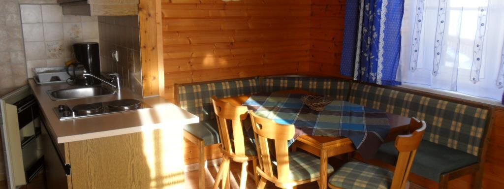 A cozy kitchen with a dining area and wooden walls. The light shines through the window, creating an inviting atmosphere. - Appt. Garni Anny - Vent