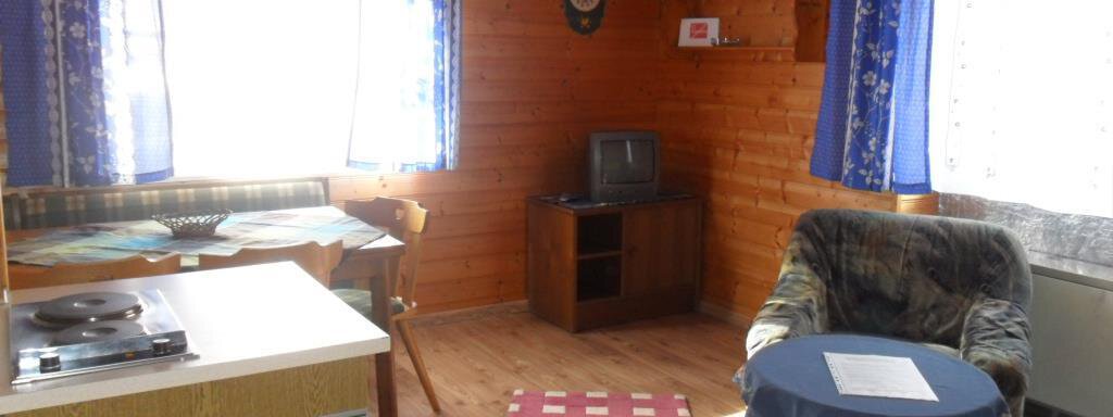 A cozy room with wooden walls and large windows. There is a small kitchenette, a table, and a comfortable armchair. - Appt. Garni Anny - Vent