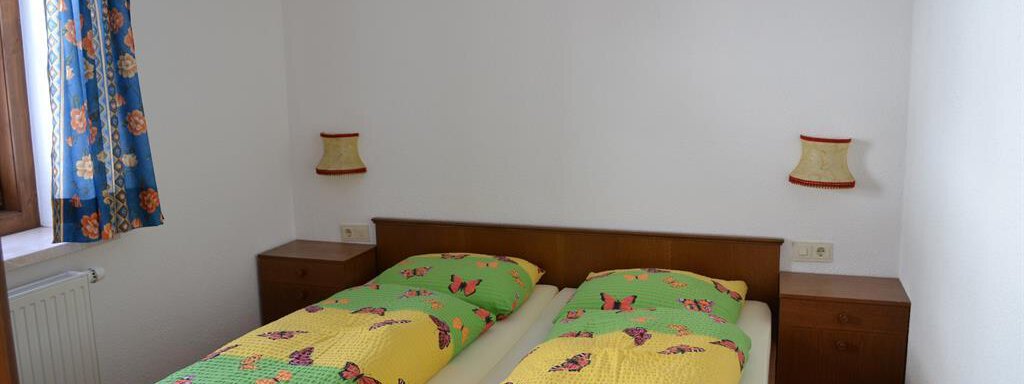 A cozy bedroom with two single beds and colorful bedspreads. Colorful curtains and bedside lamps complement the room. - Appt. Garni Anny - Vent