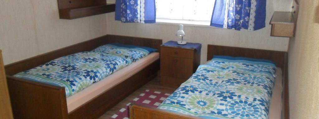 A simple bedroom with two single beds. The walls are light, and a window with blue curtains lets daylight in. - Appt. Garni Anny - Vent